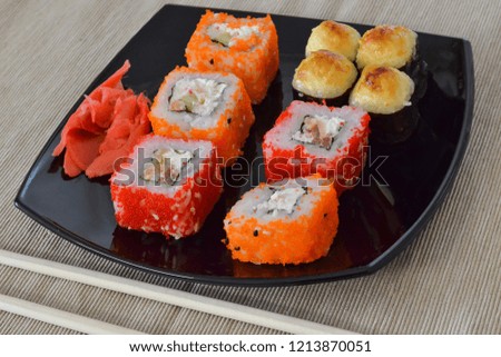 Sushi and rolls on a black plate with chopsticks.