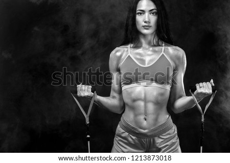 Black and white photo. Fit sports woman athlete. Workout with bands or expander in gym on black background. Copy space for fitness nutrition ads.