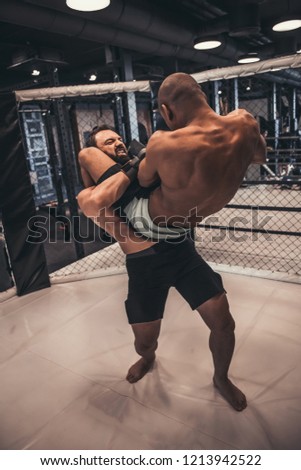 Two men in gloves and shorts are fighting in cage using grappling