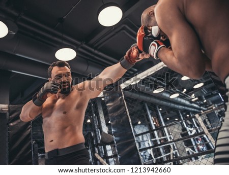 Two men in boxing gloves and shorts are fighting in cage