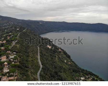 The best view of the Italian village, winding country road, view of the lake and grape fields, red tile houses, European-style, many village houses in green gardens and trees, overcast weather, Rome 