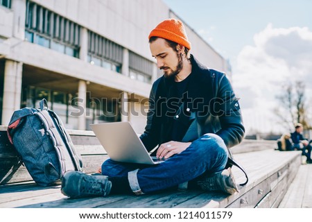 Concentrated caucasian student typing on laptop computer learning online while sitting outdoors on urban setting, skilled male freelancer checking mail and notification about business on netbook