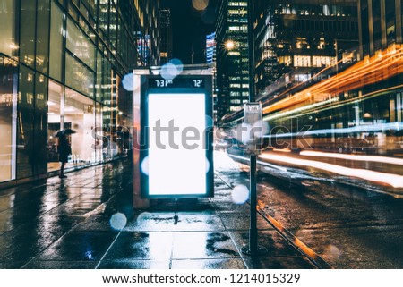Bus station billboard in rainy night with blank copy space screen for advertising or promotional content, empty mock up Lightbox for information, clear display in urban city street with long exposure