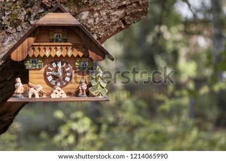 Wooden wall clock in the form of a tree house hang on the tree. On the background of bright green bushes. design element. Outdoor. In the upper left corner of the frame. 
