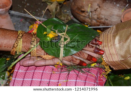 The Divine Knot / Hasta Bandhan Bond : Bride and groom's hand tied at a traditional bengali Indian wedding ceremony with jewelry and mehendi henna on a towel with leaf 