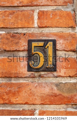 House number fifty-one 51 in pressed metal polished brass and black screwed to brickwall from Sweden or Belgium