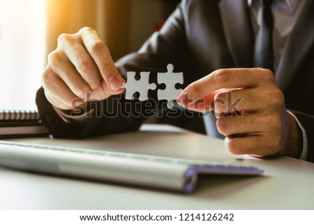 Business solutions and success concept. Businessman hand connecting jigsaw puzzle at office in morning light
