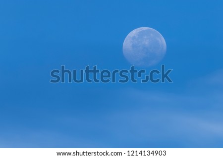 Low contrast waxing gibbous earth moon over the blue winter sky. Soft contrast of white cirrostratus cloud at lower edge of picture.