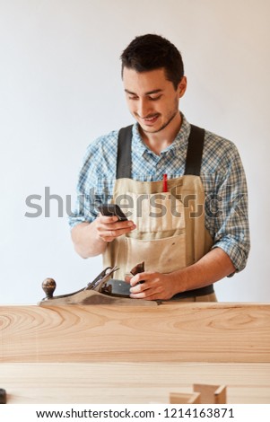 Carpenter in working wear and apron works with a planer making custom made furniture. He planes a wooden plank isolated over white background.