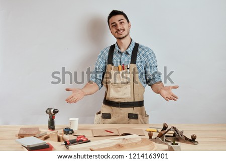 Happy cheerful cabinetmaker looking at camera standing at the table with planer and drill. DIY concept. Woodworking and crafts tools. Carpentry hand tools.