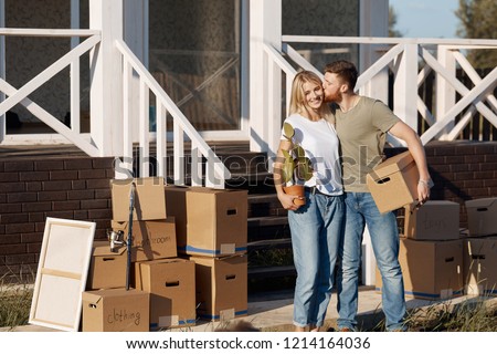 Husband and wife standing in front of new buying home with boxes. bought first home