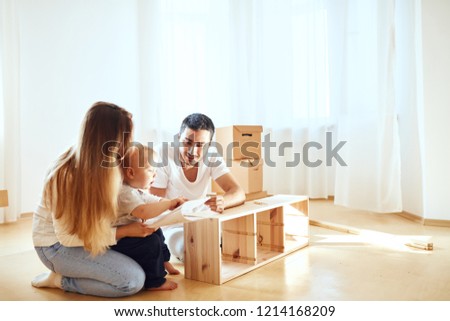family with little boy reading instruction and assemble furniture together at living room of new apartment pile of moving boxes on background