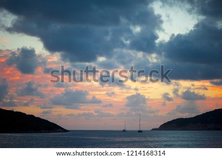 Sunset in the sea. 
Picture taken from a yacht. Two yachts sailing into a cove at sunset. 
Beautifully colored red/orange sky; hills at sides; still, calm, dark sea. 