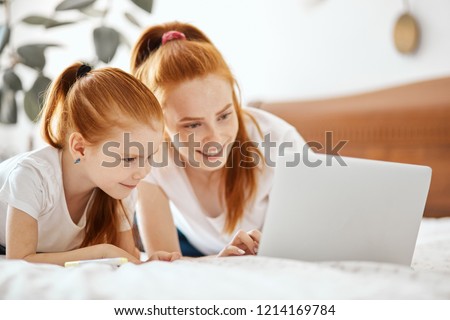 Precious time together. Lovely red-haired family watching something interesting on laptop, relaxing om bed and smiling, admiring company of each other