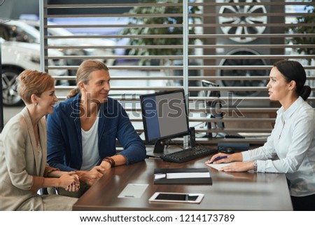 Couple of buisness people listening the conditions of rental agreement for signing, sitting at table with the female agent at car rental salon