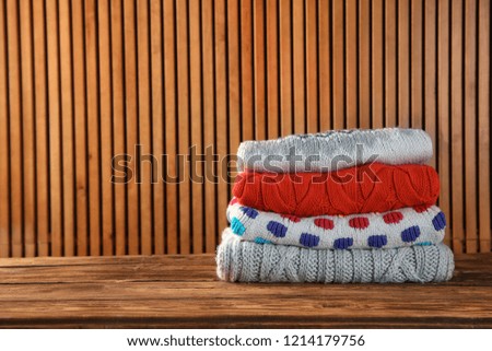 Pile of folded winter clothes on wooden table. Space for text