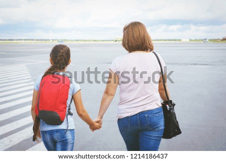 Mom with a bag and a daughter with a red backpack passengers go to the ramp of the plane on the airport field.