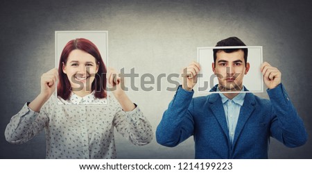 Businessman and woman covering their faces using photo sheets with happy and sad portrait emoticon, like a mask to hide the real emotion from society. Fake identity concept. Introvert vs extrovert. Royalty-Free Stock Photo #1214199223