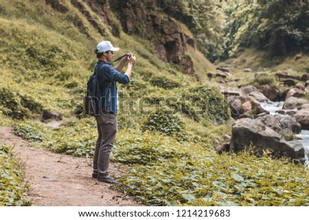 Young Asian traveler man taking photo outdoors scenic nature background. Lifestyle and relaxation concept.