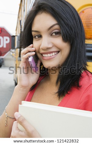 Portrait of a beautiful school student talking on cell phone with school bus in the background