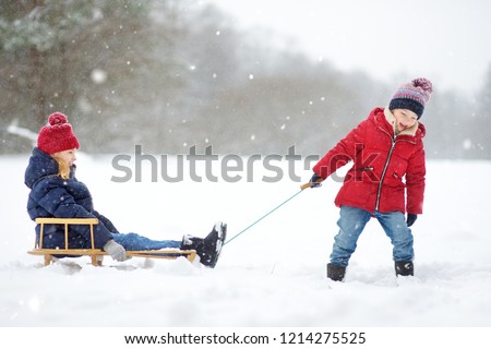 Two funny little girls having fun with a sleigh in beautiful winter park. Cute children playing in a snow. Winter activities for kids.