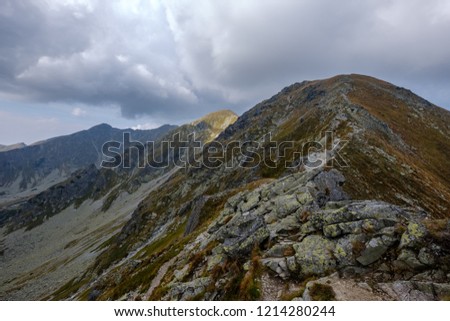 mountain panorama from top of Banikov peak in Slovakian Tatra mountains with rocky landscape and shadows of hikers in bright day with storm clouds approaching in overcast day