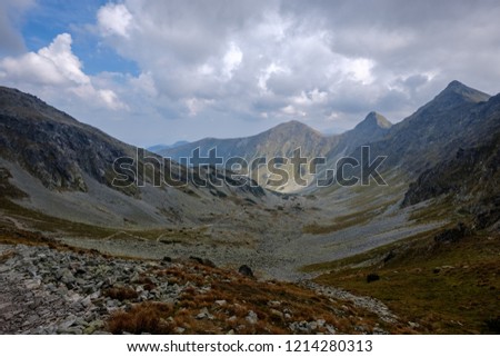 mountain panorama from top of Banikov peak in Slovakian Tatra mountains with rocky landscape and shadows of hikers in bright day with storm clouds approaching in overcast day