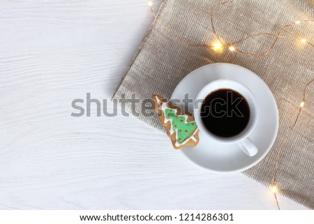 cup of black coffee with ginger cookies in the shape of a Christmas tree with festive garland on the table top view / winter Holiday warming drink