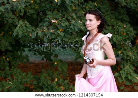 Fine emotional brunette with vintage photo camera. Young girl in vintage pink pastel with live expressions on beautiful country and old background.