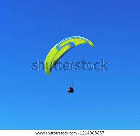Yellow blue paraglider on blue sky.