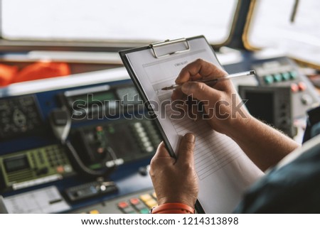 Marine navigational officer or chief mate on navigation watch on ship or vessel. He fills up checklist. Ship routine paperwork Royalty-Free Stock Photo #1214313898