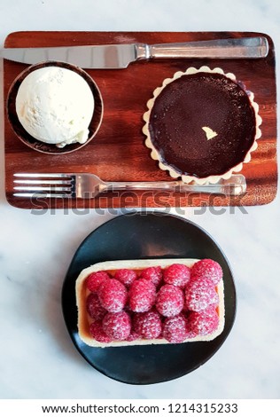 Chocolate Tart with a scoop of vanilla ice cream served on wooden plate and Raspberry Tart served on black porcelain plate.Flate lay picture.
