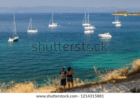 Tourists photographing beautiful bay with yachts in Porquerolles, the island in southern France. Holidays in France.