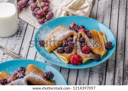 Homemade crepes with frozen berries, topped sugar, rustic wood board, vintage photography