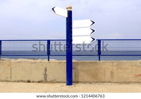 Blank directional road signs against sea and blue sky.