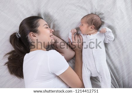 Young happy calm mother and newborn baby resting in bed together. Mom and infant kissing and hugging. Maternity, parenthood, motherhood concept, view from above