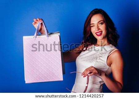Young redhead girl in white dress with shopping bags on blue background.