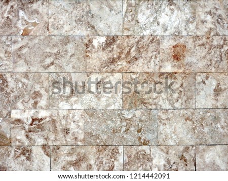 
The wall is lined with polished facing tiles of light natural stone with a beautiful pattern. Abstract background.					