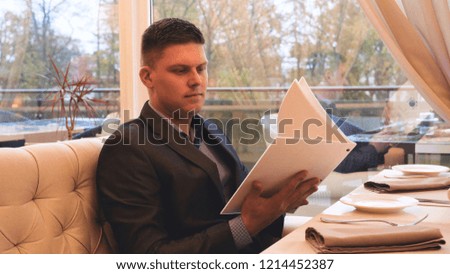 Handsome guy (man) in a suit restaurant, gets a menu. Concept of: Menu, Orders, Waiter, Business, Beautiful atmosphere, Lifestyle.