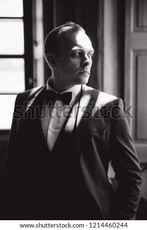 Handsome man in suit and tie bow stand near the window. Black and white picture