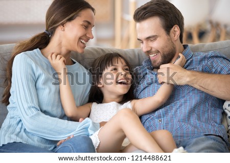 Close up smiling cheerful daughter tickling parents people have fun playtime together at home. Parents laughing enjoy weekend with little adorable kid. Happy parenting love friendly relations concept Royalty-Free Stock Photo #1214488621