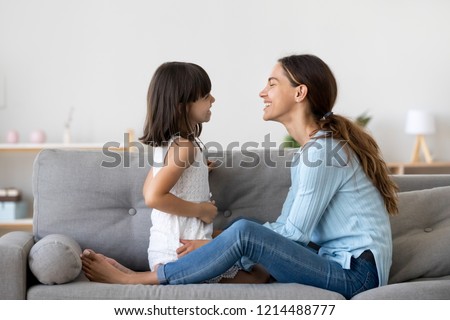 Attractive woman and little girl sitting on comfortable couch at home. Young mother talking communicates with small adorable daughter. Best friends happy motherhood weekend together with kid concept Royalty-Free Stock Photo #1214488777