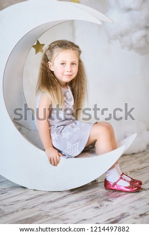 dreamy girl sitting on a wooden decorative moon in the clouds and stars. childhood concept. belief in fairy tales