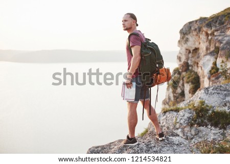 Attractive man with map enjoying the view of the mountains landscape above the water surface. Travel Lifestyle adventure vacations concept.