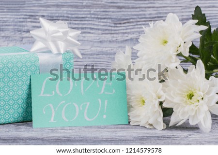 Gift box, flowers and love message. Close up beautiful chrysanthemums, gift and card with inscription love you on wooden background. Romantic holiday background.