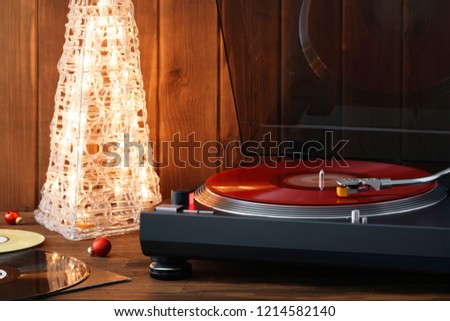 Christmas picture. The rotating moment of a red vinyl record on the turntable, the stylus with a needle falls on vinyl, music on the background of a glowing Christmas tree with red glass balls