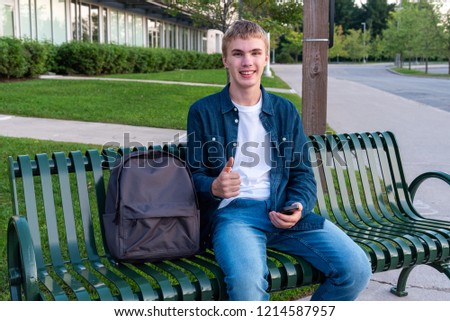 Happy male teenager texting while sitting on a bench.
