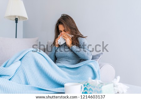 Sick Woman.Flu.Woman Caught Cold. Sneezing into Tissue. Headache. Virus .Medicines. Young Woman Infected With Cold Blowing Her Nose In Handkerchief. Sick woman with a headache sitting on a sofa  Royalty-Free Stock Photo #1214603137