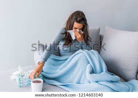Sick woman with headache sitting under the blanket. Sick woman with seasonal infections, flu, allergy lying in bed. Sick woman covered with a blanket lying in bed with high fever and a flu, resting.  Royalty-Free Stock Photo #1214603140