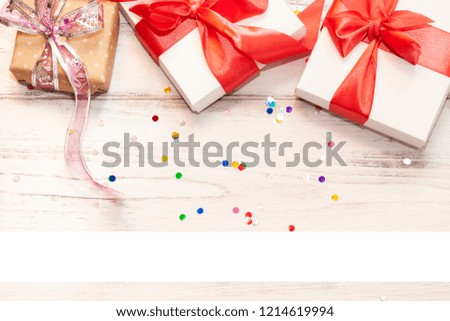 One brown gift box and two white paper boxes with red ribbon on white wooden board background with space for text.